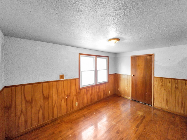 unfurnished room with wooden walls, a textured ceiling, and hardwood / wood-style floors