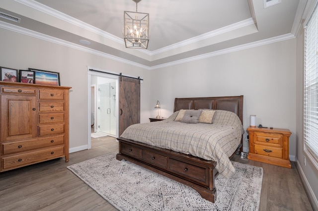 bedroom with hardwood / wood-style flooring, a barn door, a tray ceiling, ornamental molding, and a chandelier