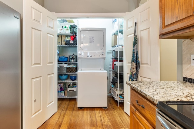 laundry room with stacked washer and dryer and light hardwood / wood-style flooring