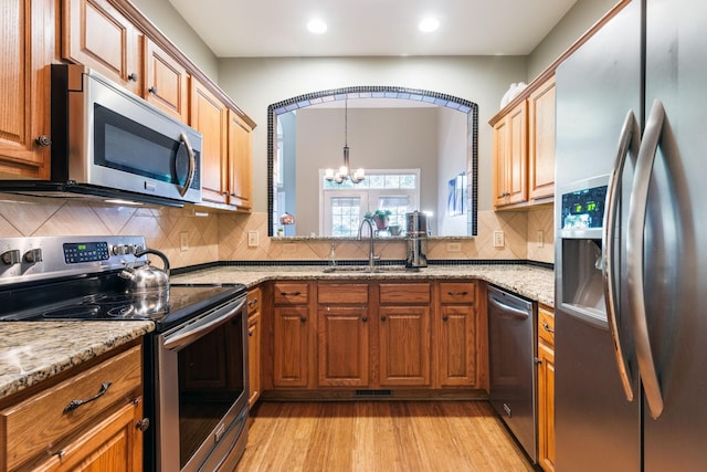 kitchen with appliances with stainless steel finishes, a chandelier, sink, light hardwood / wood-style floors, and light stone countertops