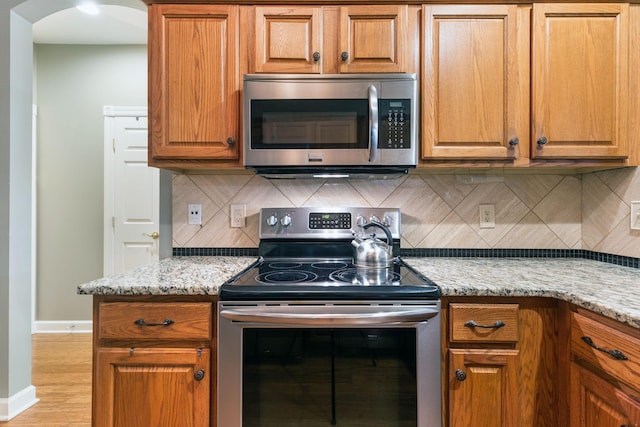 kitchen featuring decorative backsplash, stainless steel appliances, light stone countertops, and light hardwood / wood-style flooring