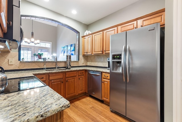 kitchen with light wood-type flooring, stainless steel appliances, light stone countertops, sink, and decorative backsplash