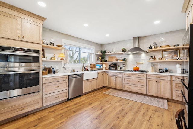 kitchen with appliances with stainless steel finishes, tasteful backsplash, light brown cabinetry, wall chimney exhaust hood, and sink