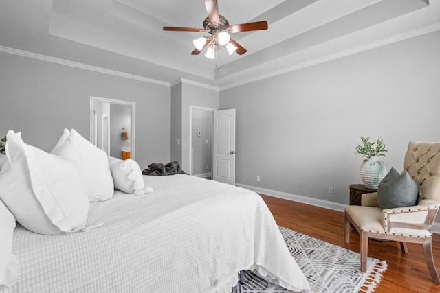 bedroom with wood-type flooring, connected bathroom, ceiling fan, crown molding, and a raised ceiling