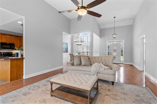 living room with light wood-type flooring, a high ceiling, and ceiling fan with notable chandelier