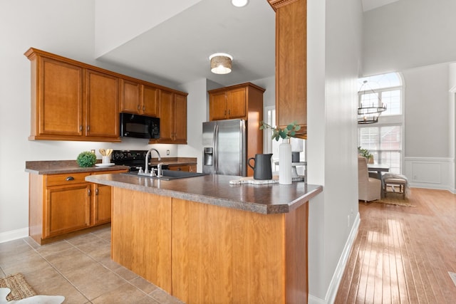 kitchen with sink, a towering ceiling, light hardwood / wood-style floors, black appliances, and kitchen peninsula