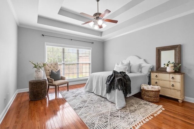 bedroom featuring ceiling fan, hardwood / wood-style flooring, a tray ceiling, and ornamental molding