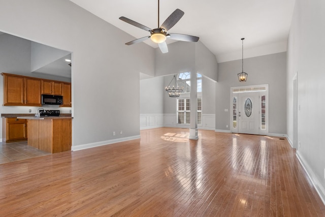 unfurnished living room with ceiling fan with notable chandelier, light hardwood / wood-style flooring, and a towering ceiling