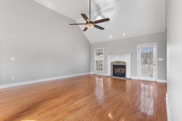 unfurnished living room featuring light hardwood / wood-style flooring, high vaulted ceiling, a wealth of natural light, and a tiled fireplace