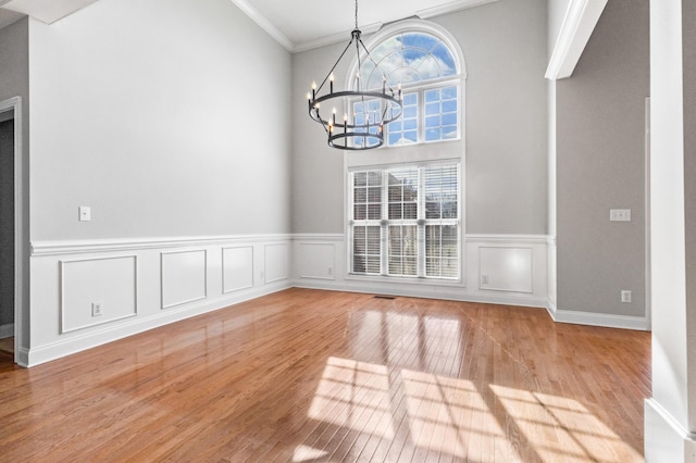 unfurnished dining area featuring light wood-type flooring, plenty of natural light, crown molding, and a chandelier