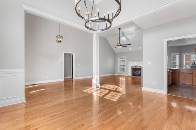 unfurnished living room with ceiling fan with notable chandelier, light wood-type flooring, vaulted ceiling, and ornamental molding