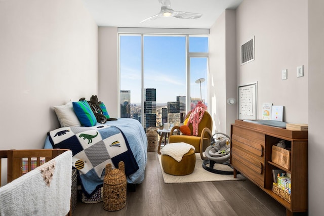 bedroom with visible vents, a city view, a ceiling fan, wood finished floors, and floor to ceiling windows