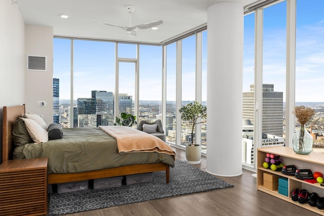 bedroom with a city view, wood finished floors, visible vents, and expansive windows
