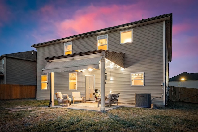 back house at dusk with a yard, a patio area, and central AC unit