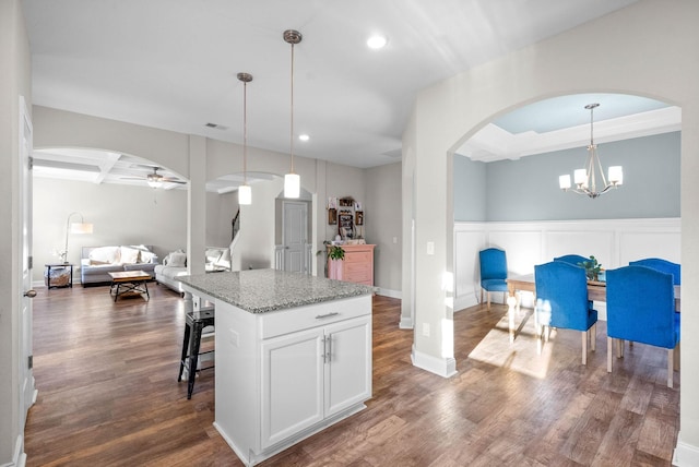 kitchen with a center island, hanging light fixtures, light stone counters, white cabinets, and ceiling fan with notable chandelier