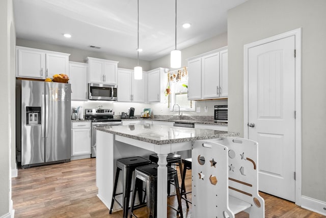 kitchen with appliances with stainless steel finishes, hanging light fixtures, a breakfast bar area, a kitchen island, and white cabinetry