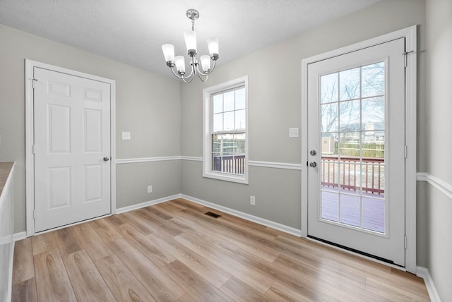 doorway with light hardwood / wood-style floors, a textured ceiling, and a notable chandelier