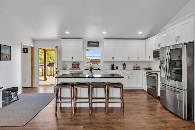 kitchen with appliances with stainless steel finishes, a breakfast bar, a center island, dark hardwood / wood-style flooring, and white cabinetry