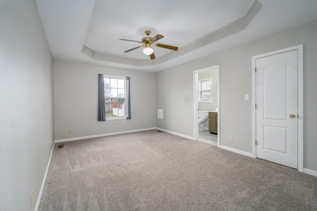 unfurnished bedroom featuring connected bathroom, light colored carpet, visible vents, baseboards, and a tray ceiling