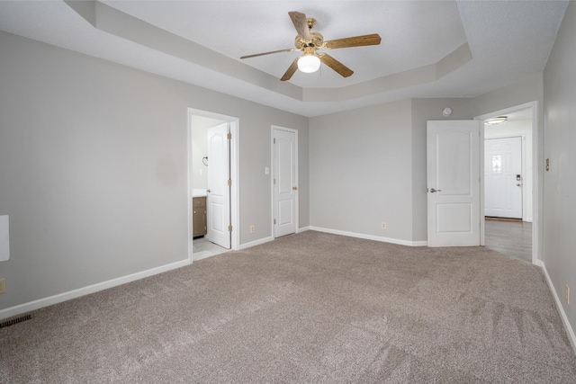 unfurnished bedroom with light carpet, visible vents, baseboards, a raised ceiling, and ensuite bathroom