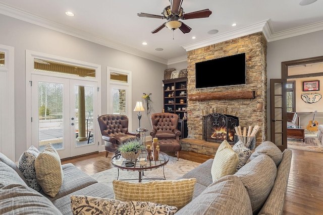 living room featuring wood-type flooring, a stone fireplace, ceiling fan, french doors, and ornamental molding