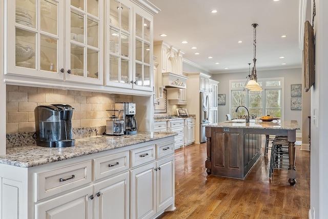 kitchen with a center island with sink, hanging light fixtures, light stone countertops, and white cabinets