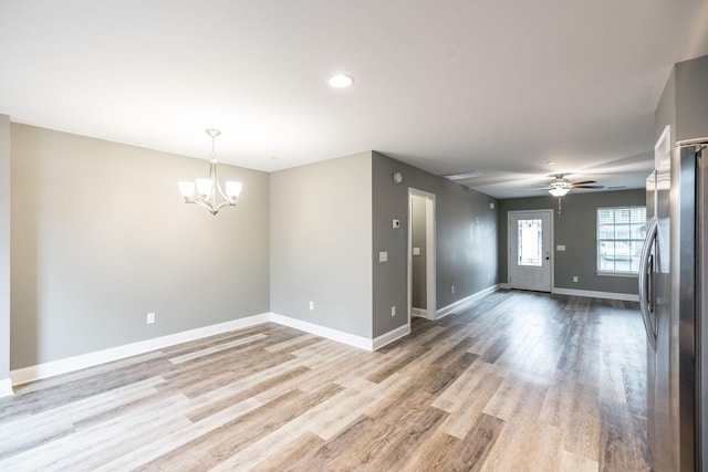 empty room with ceiling fan with notable chandelier and light wood-type flooring