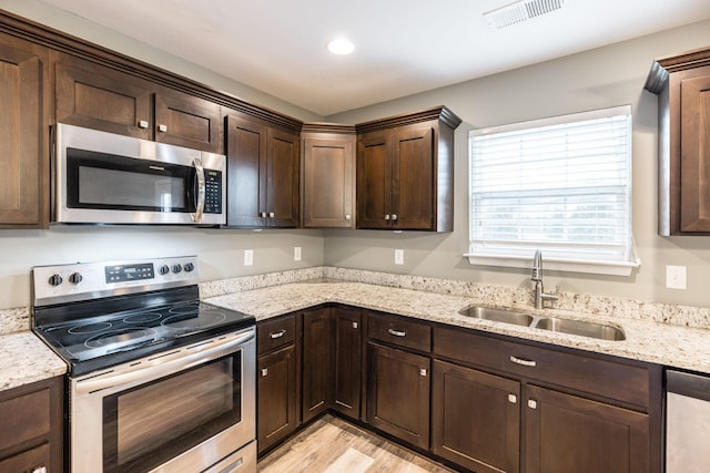 kitchen with dark brown cabinetry, appliances with stainless steel finishes, sink, and light stone countertops