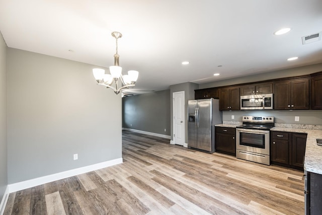 kitchen with stainless steel appliances, light hardwood / wood-style floors, dark brown cabinets, light stone counters, and pendant lighting