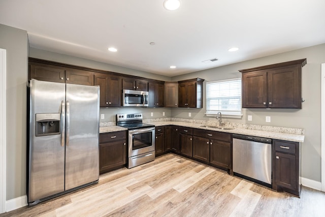 kitchen with light wood-type flooring, dark brown cabinetry, stainless steel appliances, light stone countertops, and sink