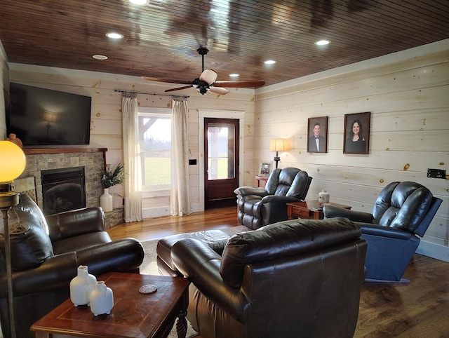 living room featuring wood ceiling, wood walls, a stone fireplace, ceiling fan, and hardwood / wood-style floors