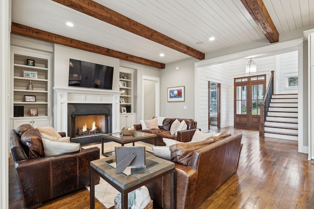 living area featuring dark wood-style floors, a lit fireplace, stairs, and built in features