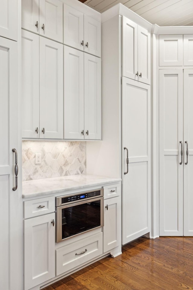 kitchen with light stone counters, oven, dark wood-style flooring, white cabinets, and backsplash