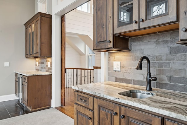 kitchen with dark tile patterned floors, a sink, light countertops, decorative backsplash, and glass insert cabinets