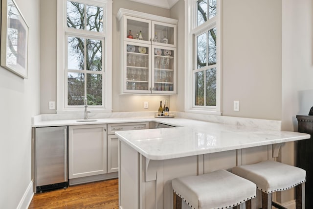 kitchen featuring light wood-style flooring, a peninsula, white cabinets, a kitchen breakfast bar, and glass insert cabinets