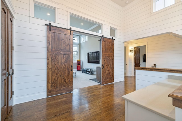 interior space with a barn door, wooden walls, a high ceiling, and dark wood-type flooring