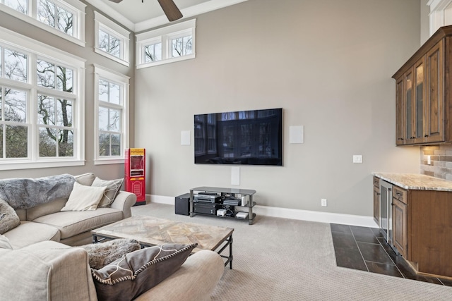 living area with ceiling fan, dark colored carpet, a high ceiling, and baseboards