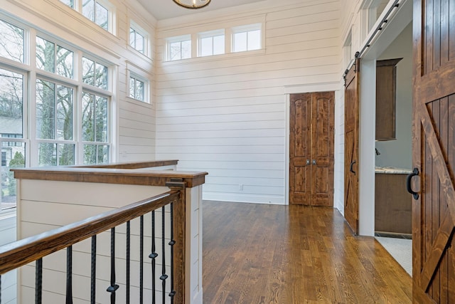 hall featuring dark wood-style floors, a barn door, wood walls, and an upstairs landing