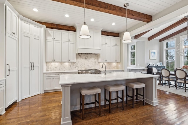 kitchen featuring a breakfast bar, a kitchen island with sink, white cabinetry, and pendant lighting