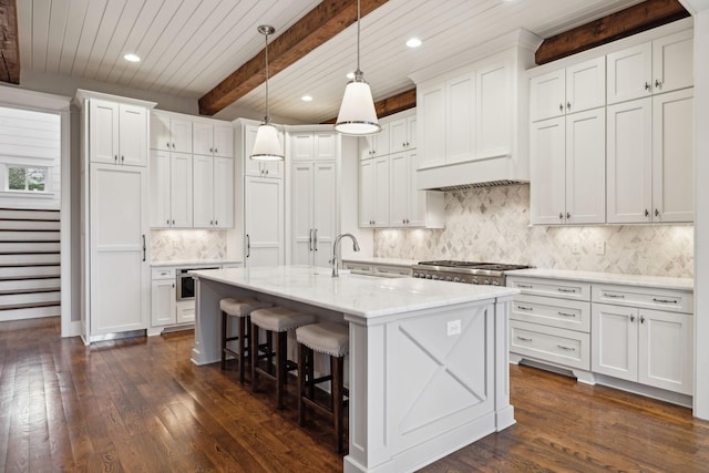 kitchen featuring a center island with sink, white cabinets, dark wood-style floors, decorative light fixtures, and a sink