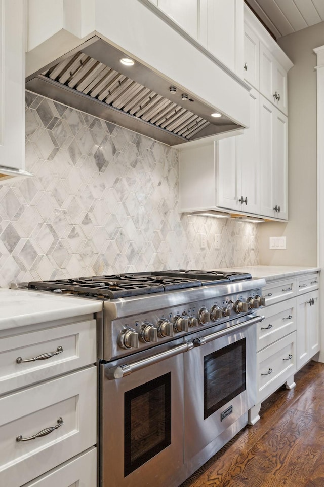 kitchen with white cabinets, dark wood-style floors, light countertops, wall chimney range hood, and double oven range