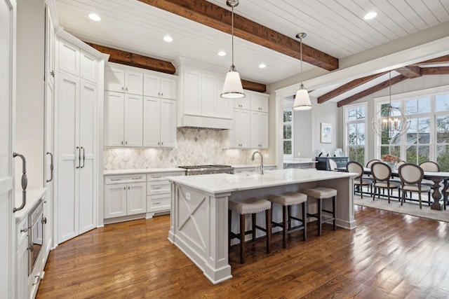 kitchen featuring light countertops, an island with sink, decorative light fixtures, and white cabinets