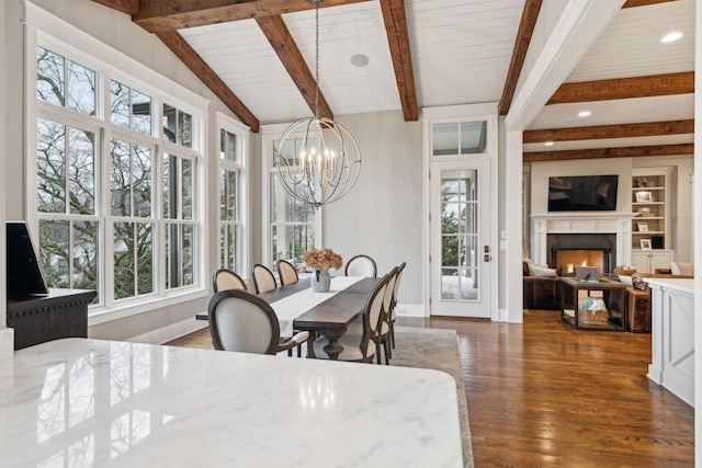 dining space featuring a warm lit fireplace, baseboards, lofted ceiling with beams, dark wood-style flooring, and a chandelier