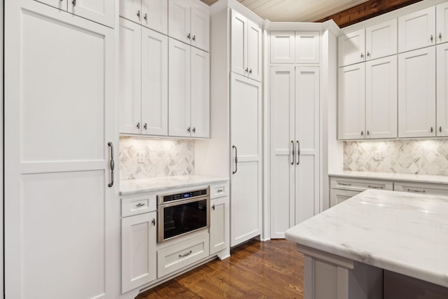 kitchen featuring decorative backsplash, light stone counters, dark wood-type flooring, oven, and white cabinetry