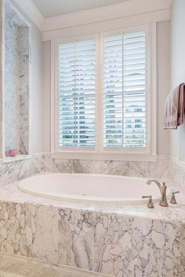 bathroom with ornamental molding, a wealth of natural light, and a tub with marble appearance