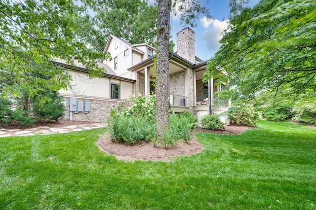 exterior space with a lawn, stone siding, a chimney, a porch, and stucco siding