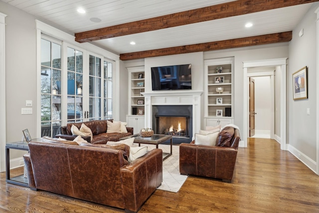 living area with a lit fireplace, baseboards, beam ceiling, and wood finished floors