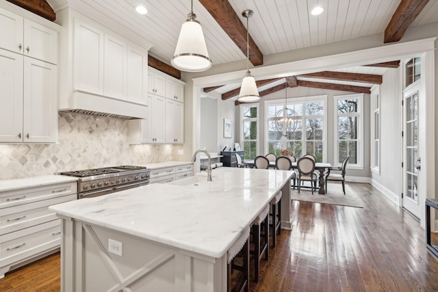 kitchen featuring white cabinets, range with two ovens, a kitchen island with sink, and decorative light fixtures