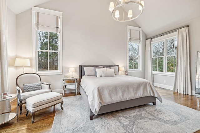 bedroom featuring lofted ceiling, baseboards, wood finished floors, and a notable chandelier