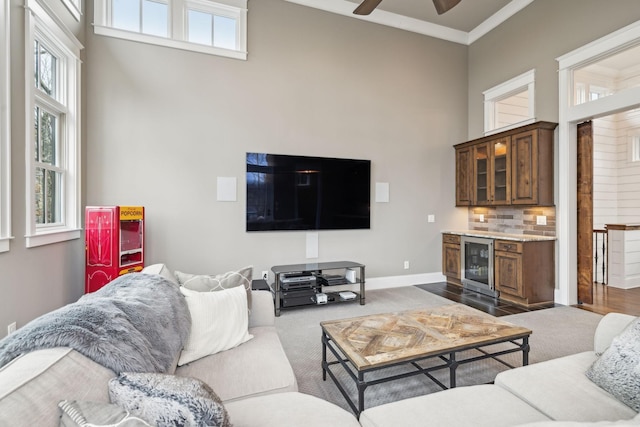 living area featuring baseboards, a towering ceiling, ceiling fan, wine cooler, and crown molding